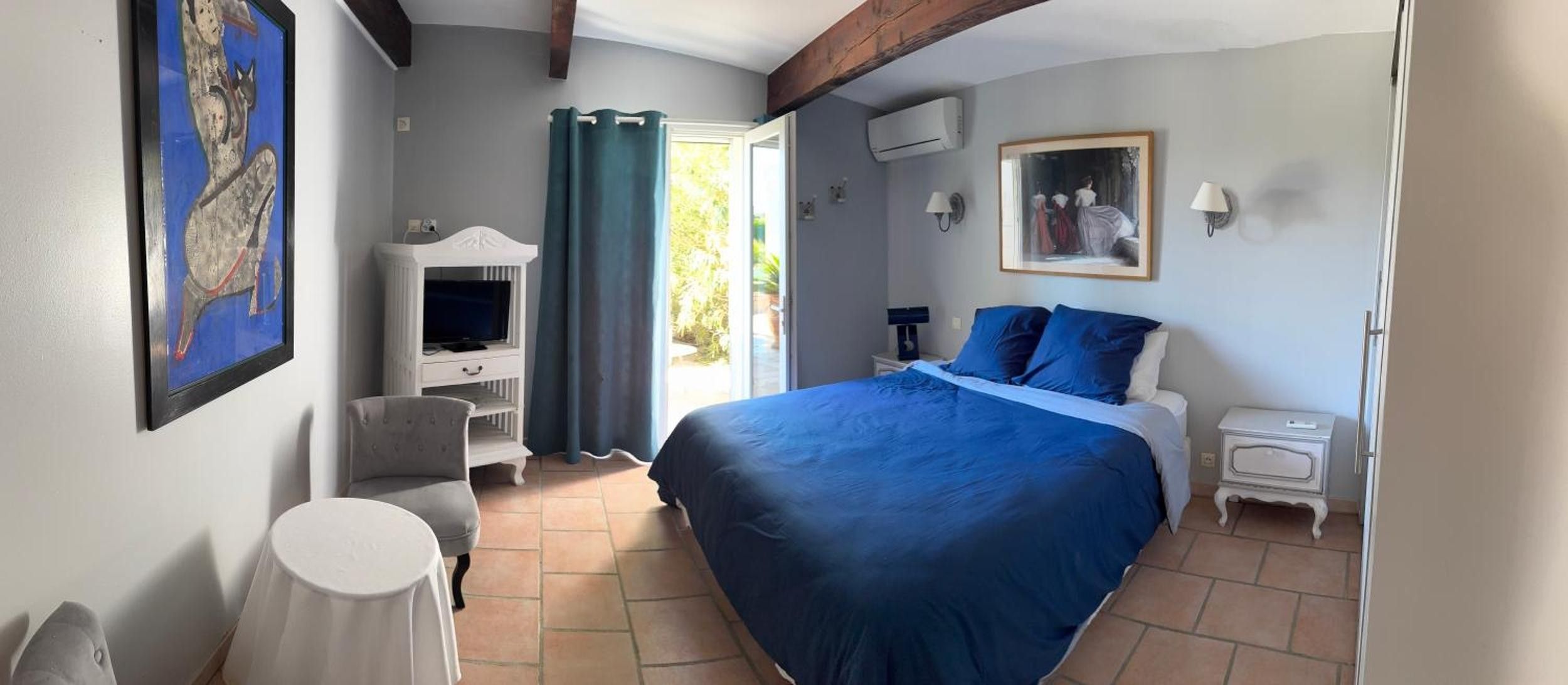 Un dormitorio con una cama grande, televisor, una silla y un cuadro en la pared.