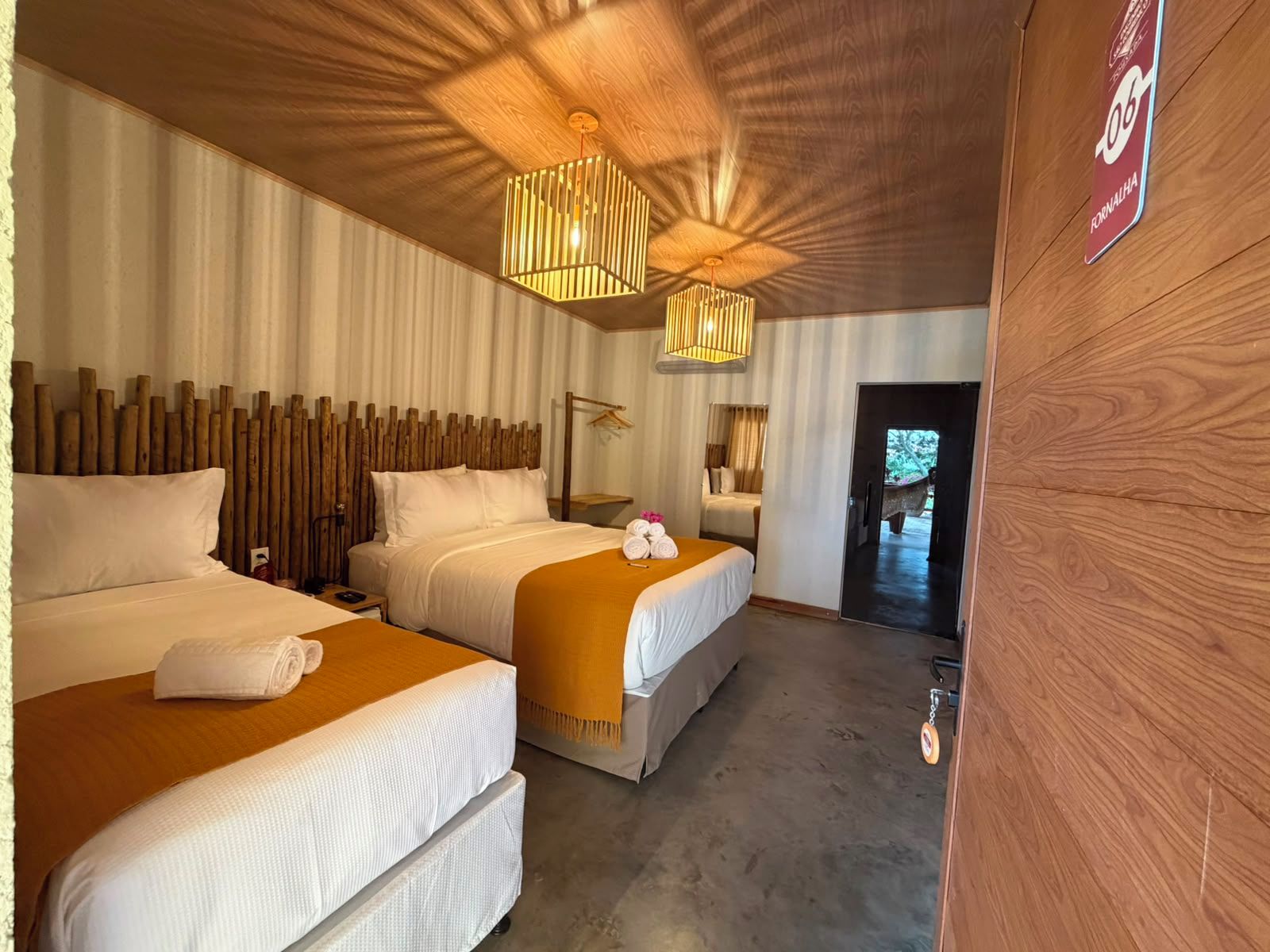 Habitación de hotel con dos camas, un cabecero de madera, un aplique de techo y una puerta que da a un pasillo.