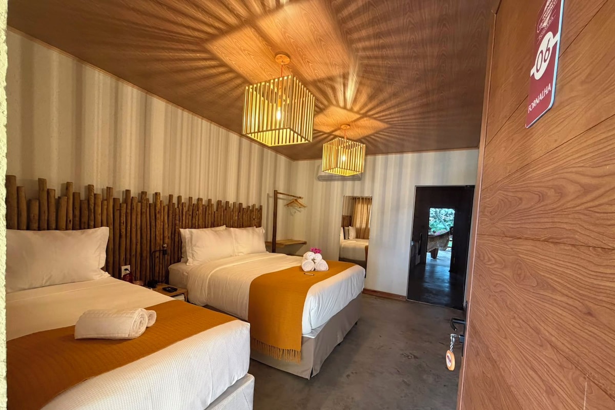 A hotel room with two beds, a wooden headboard, a ceiling light fixture, and a door leading to a corridor.