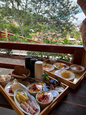 A breakfast buffet with various food items and condiments on wooden trays, set on a balcony with a view of a residential area. - Pousada Engenho (Água Branca)
