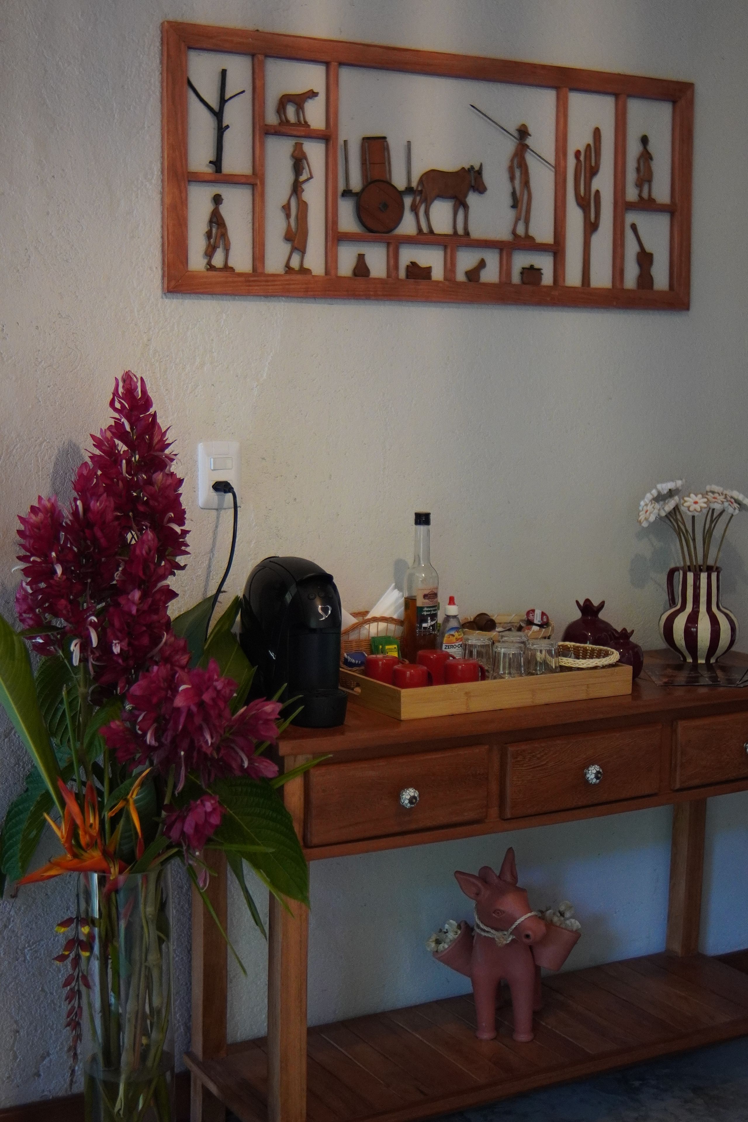 Un bureau en bois, une machine à café, un vase avec des fleurs et une statuette de cochon décorative.