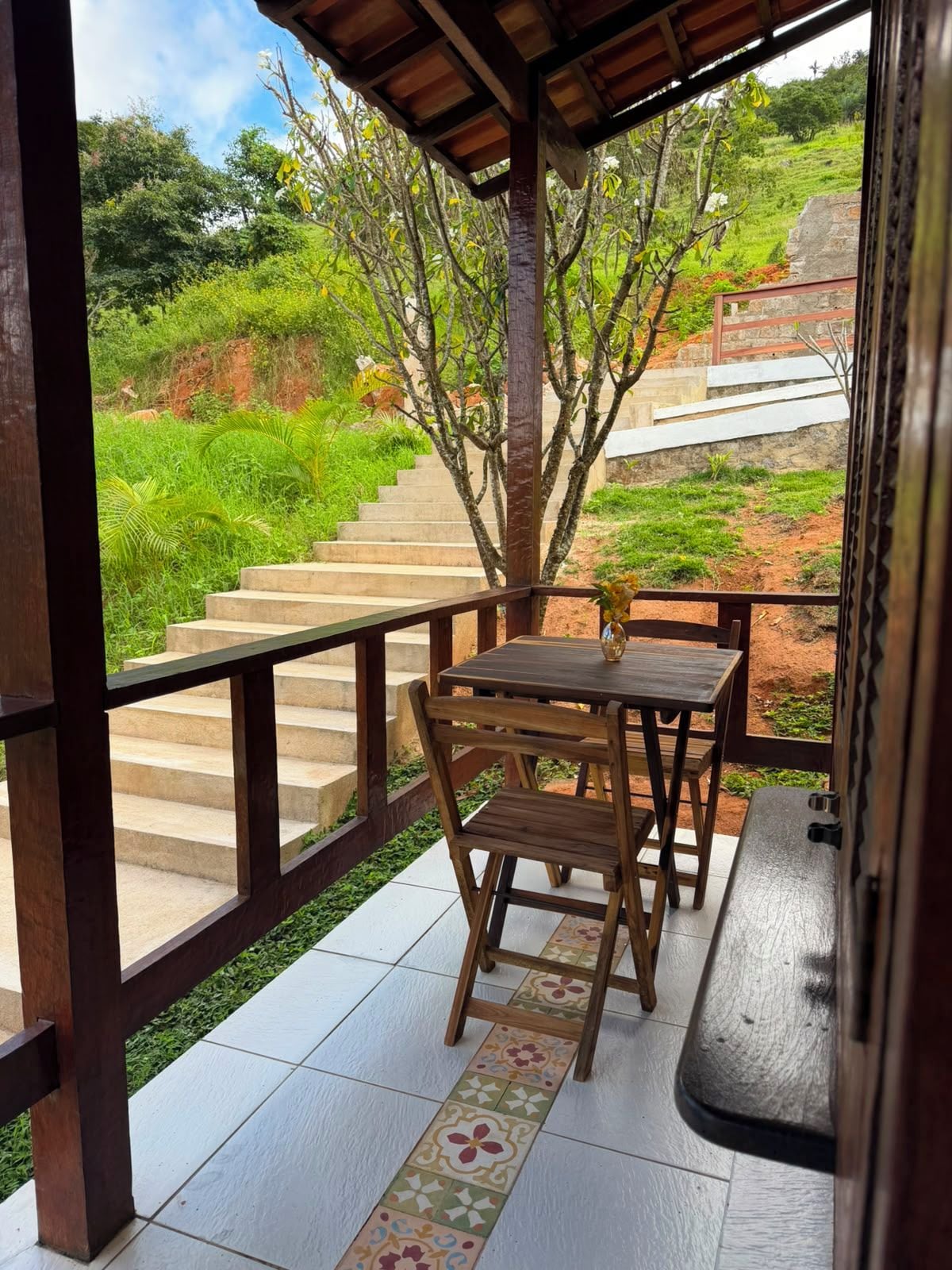 Un área de estar al aire libre cubierta con una mesa, sillas, un banco de madera y vistas a una escalera que sube por una colina.