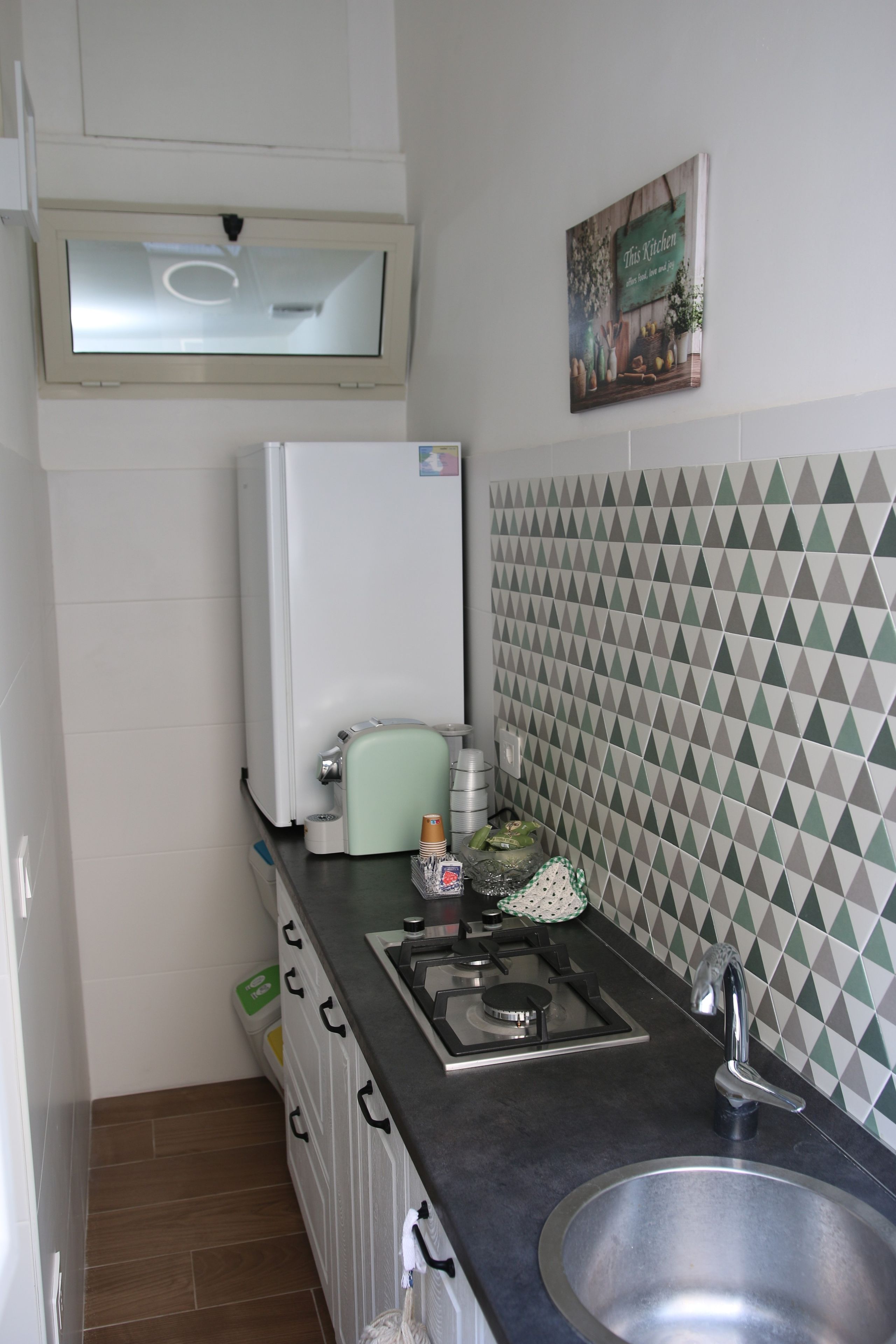Een kleine keuken met een koelkast, een koffieapparaat, een spoelbak en een decoratieve spatwand.