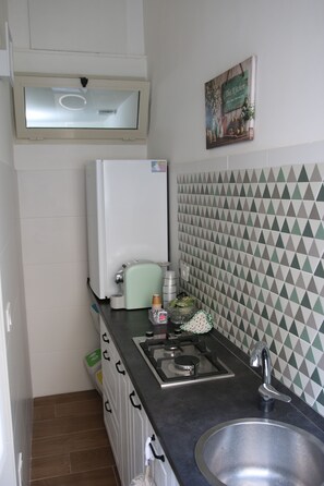 Ett kompakt kök med kylskåp, kaffemaskin, diskho och ett mönstrat stänkskydd.