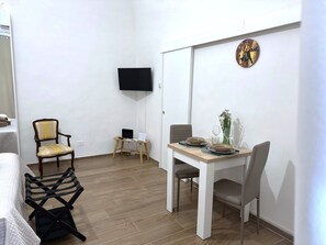 Ett litet rum med en säng, ett litet bord med stolar, en tv som är monterad på väggen och en klocka.