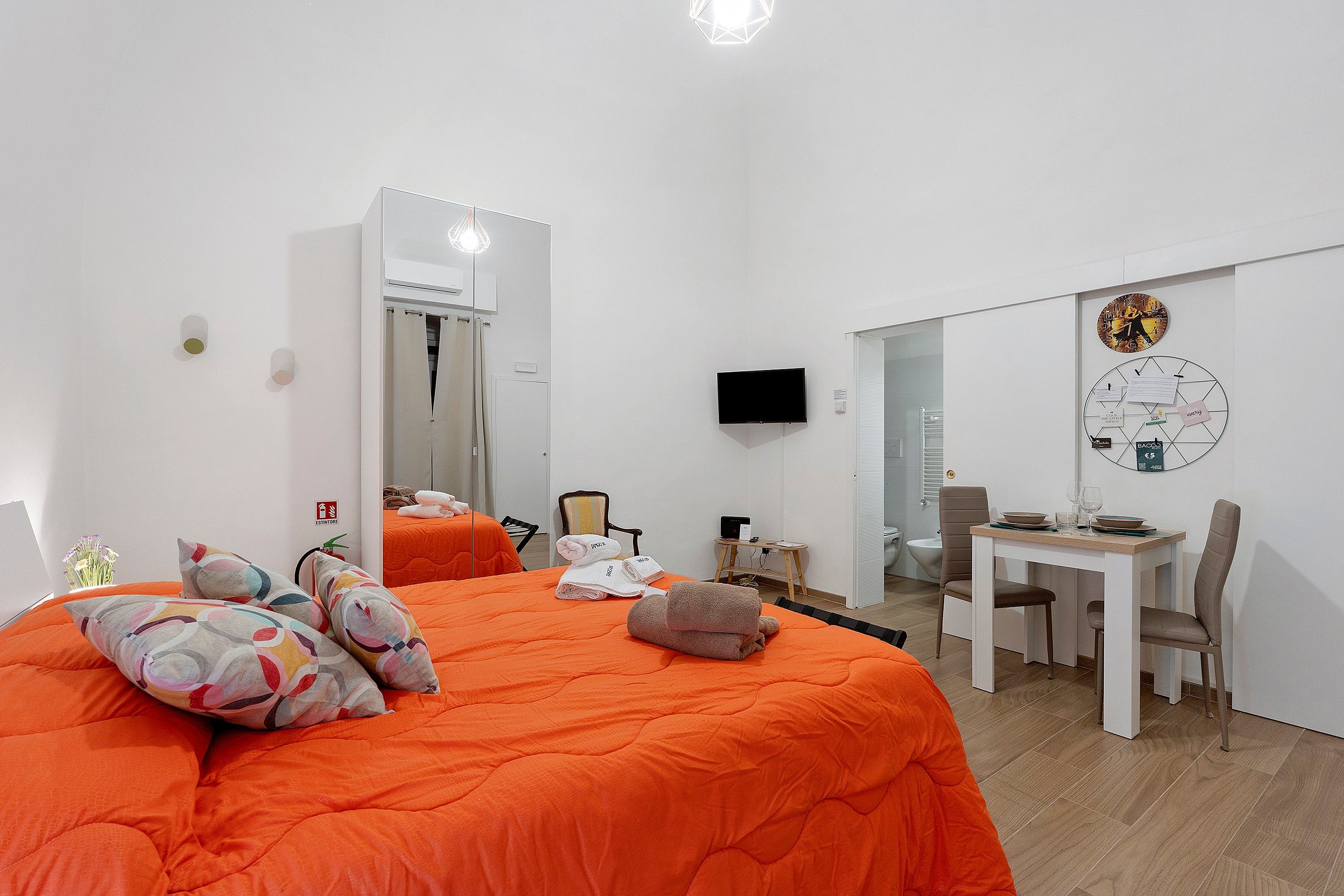Ein Hotelzimmer mit einem großen Bett, einem Schreibtisch mit Stuhl, einem Fernseher und einer Wanduhr.