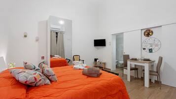 Ein Hotelzimmer mit einem großen Bett, einem Schreibtisch mit Stuhl, einem Fernseher und einer Wanduhr.