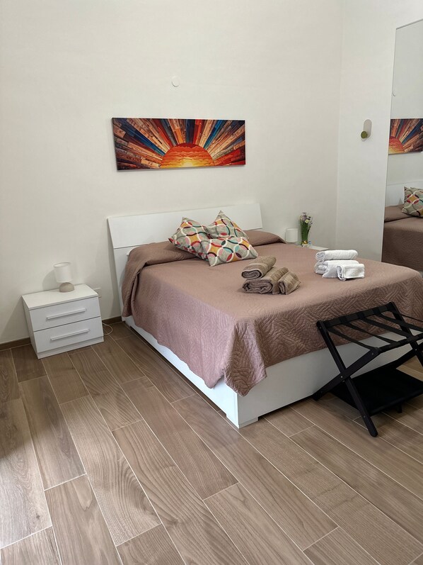 Ein ordentlich eingerichtetes Schlafzimmer mit einem Bett, Kissen, einem Nachttisch und einem Wandbild.