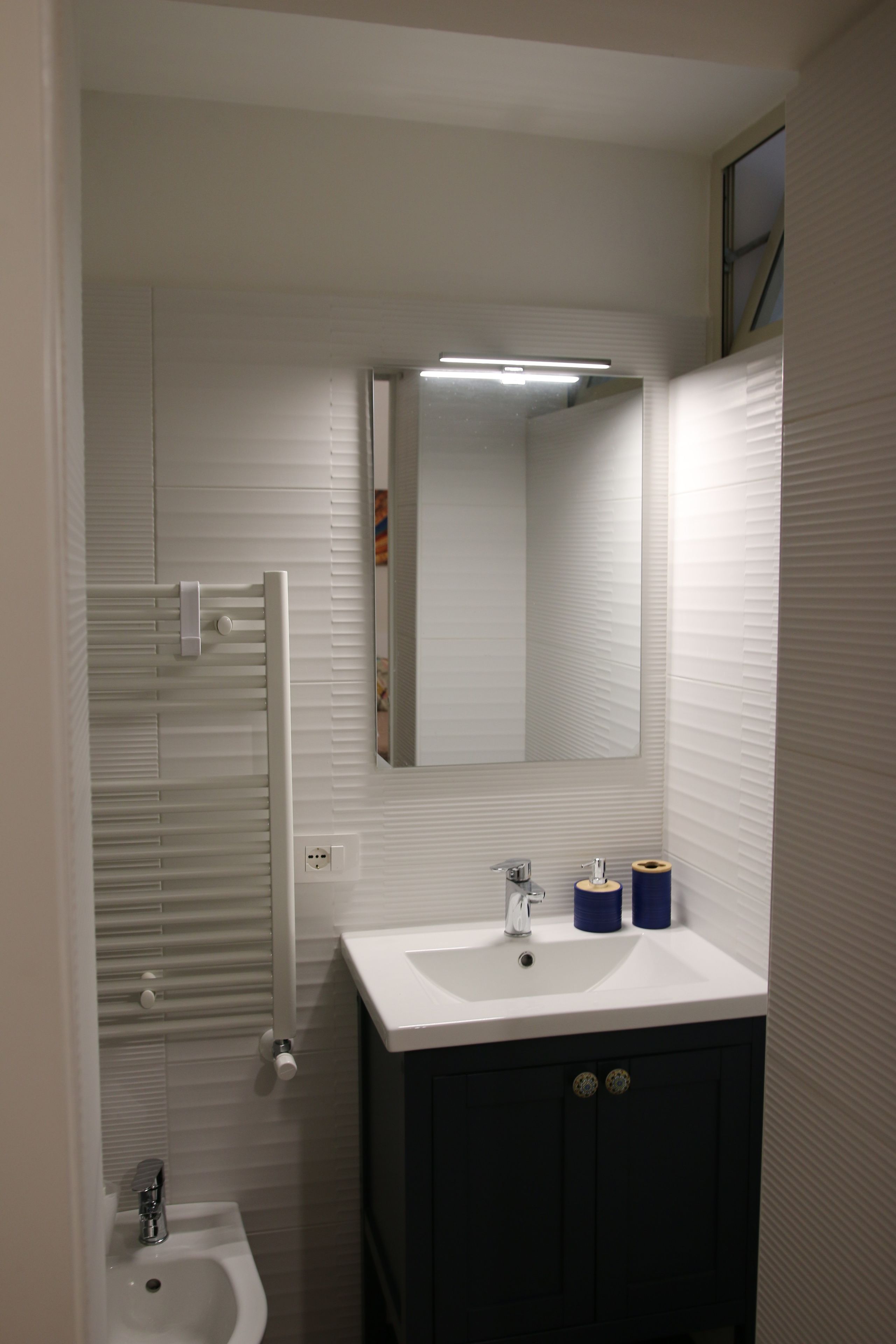 Un baño con un lavabo blanco, un espejo y un perchero para toallas.