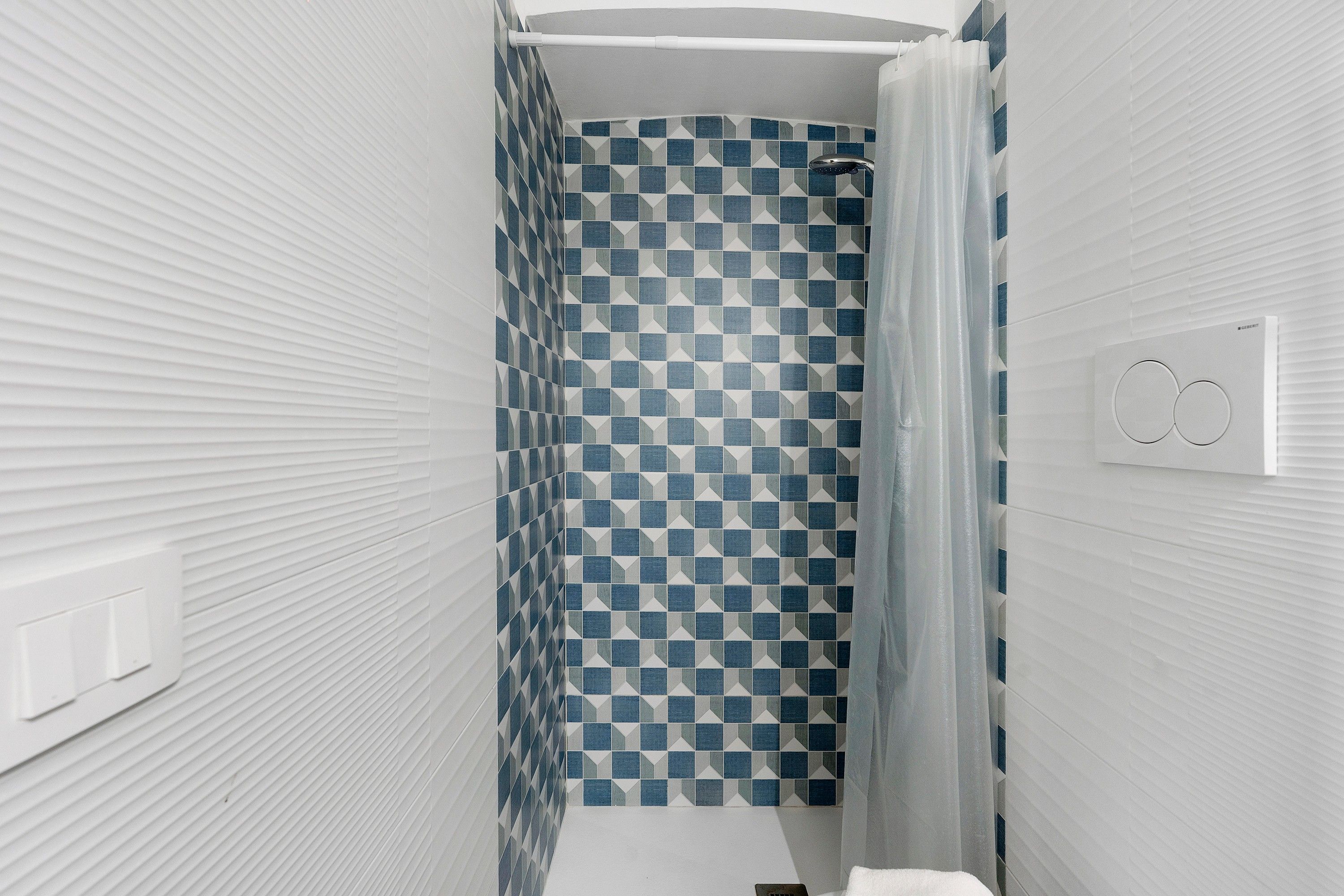 Une salle de bain avec un rideau de douche à motifs géométriques, une serviette blanche et un interrupteur visible.