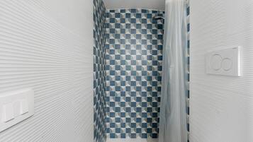 Une salle de bain avec un rideau de douche à motifs géométriques, une serviette blanche et un interrupteur visible.