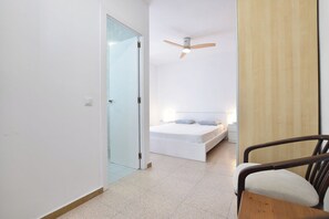 Un dormitori amb un llit, un ventilador de sostre, una porta de fusta i una cadira.