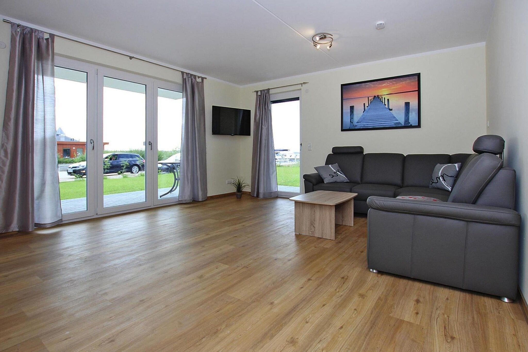 A modern living room with a grey sofa, a wooden coffee table, and a TV mounted on the wall.