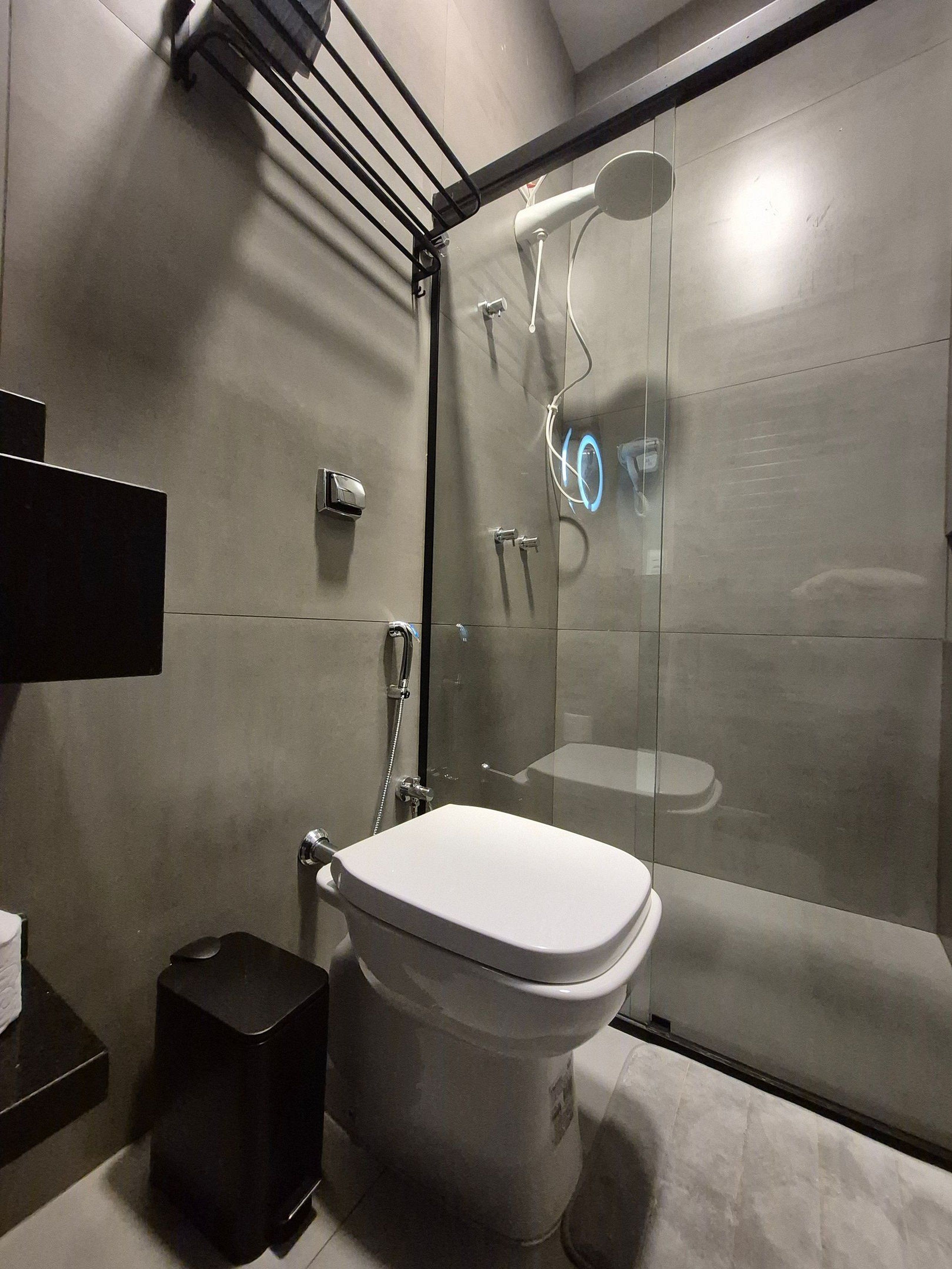 Un bagno moderno con doccia vetrata, un water bianco e un cestino nero.