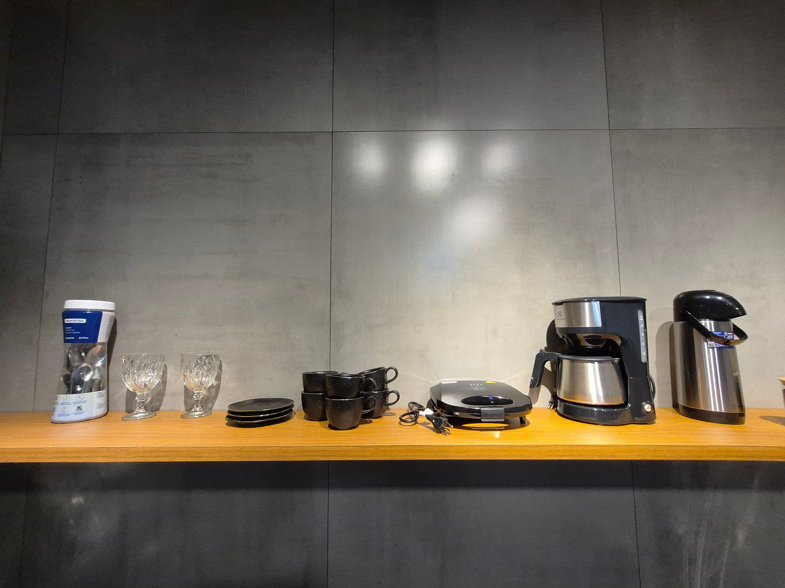 Un bancone cucina con una macchina da caffè, una termose, tazze e un vasetto di utensili.