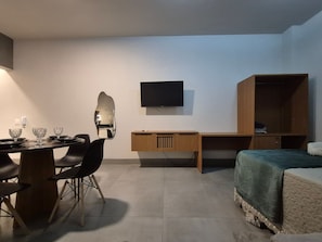 Una habitación con cama, escritorio, silla, espejo y televisor.