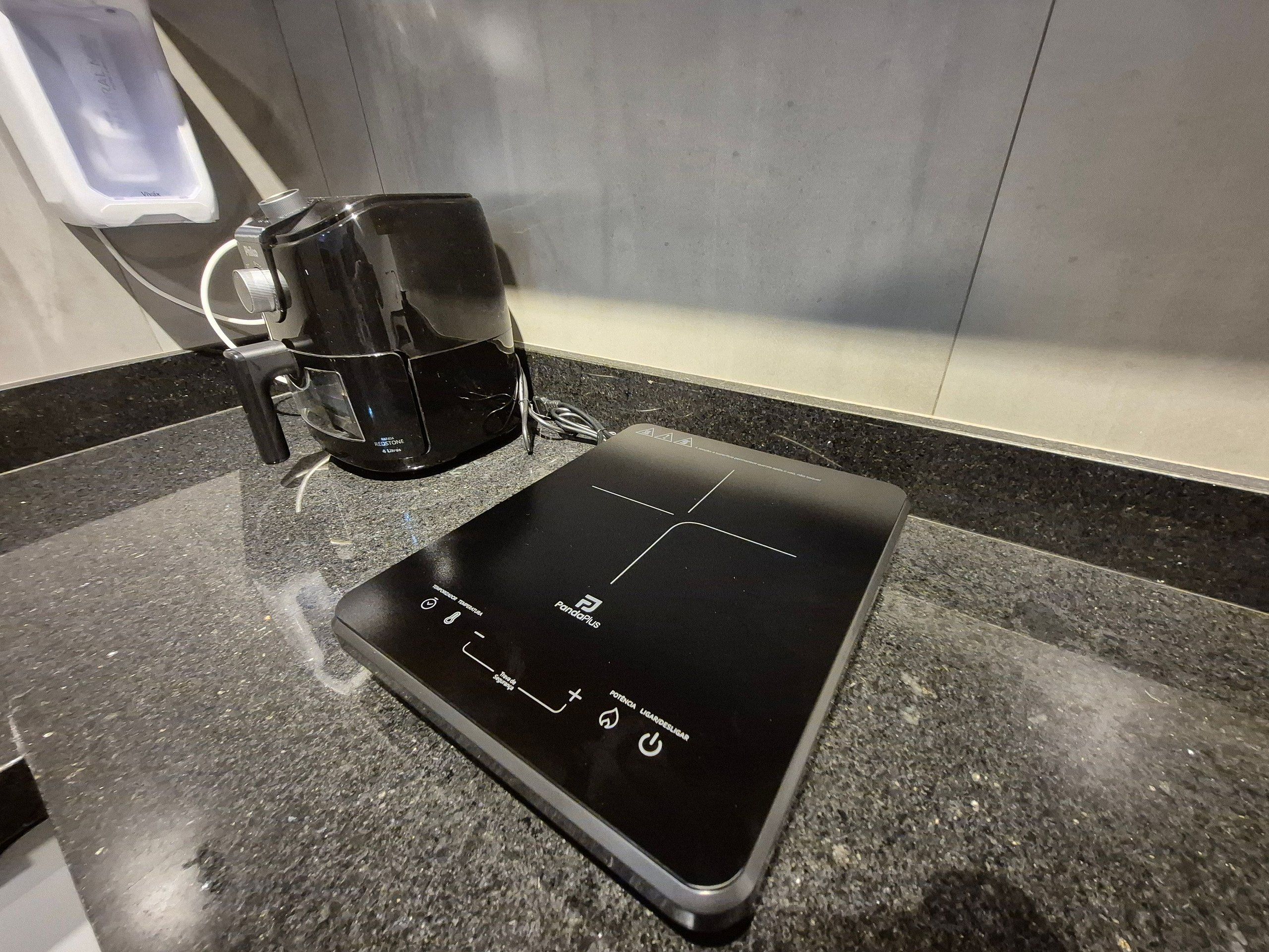 A black induction cooktop on a granite countertop with a coffee maker to its left.