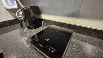 A black induction cooktop on a granite countertop with a coffee maker to its left.