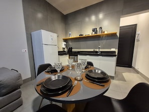 Cocina moderna con comedor, equipada con refrigerador, cafetera y estante con utensilios de cocina.