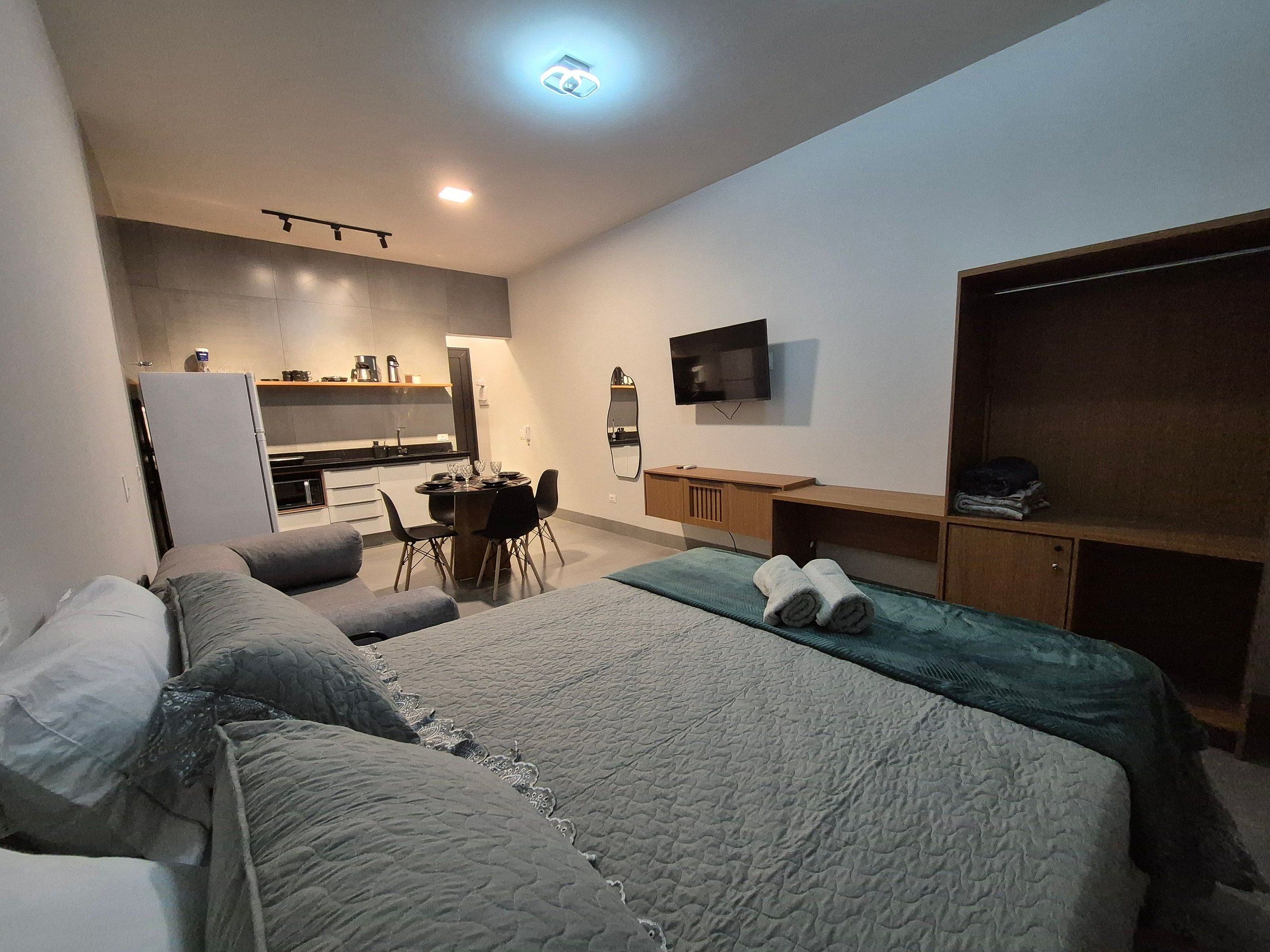 A hotel room with a bed, a desk, a chair, a television, and a kitchenette.