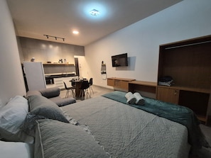 Habitación de hotel con cama, escritorio, silla, televisión y kitchenette.