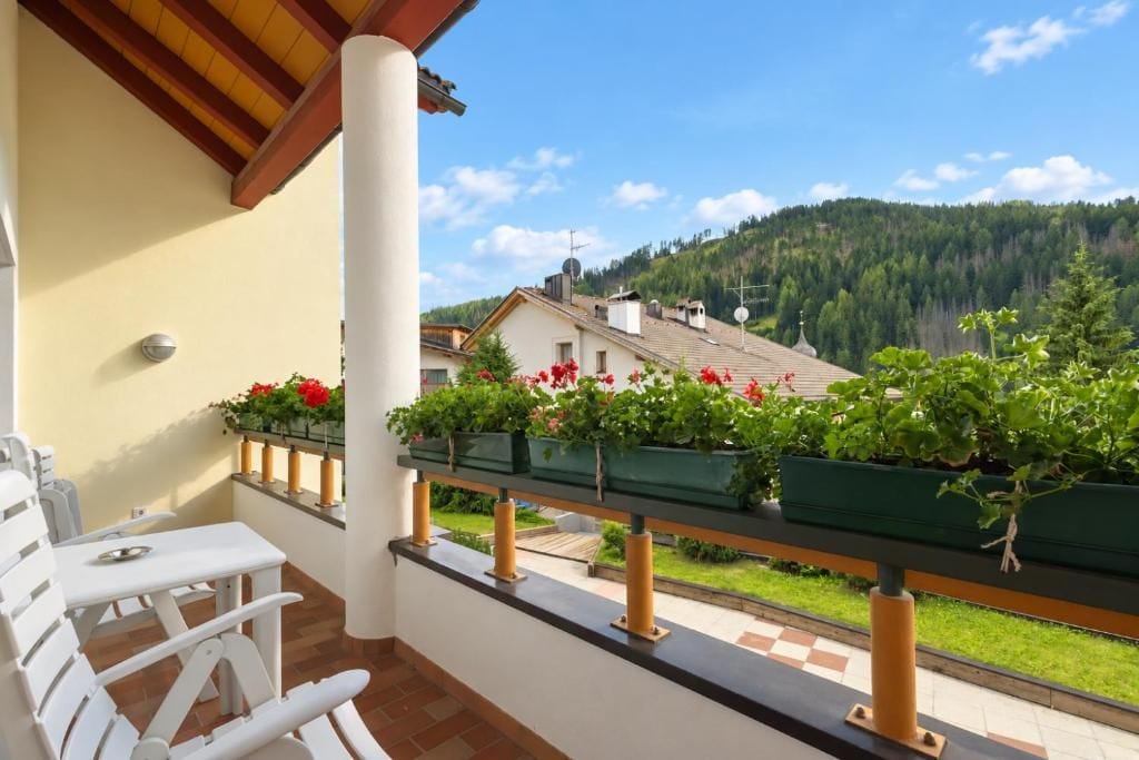 A balcony with a view of a house and forested hills.