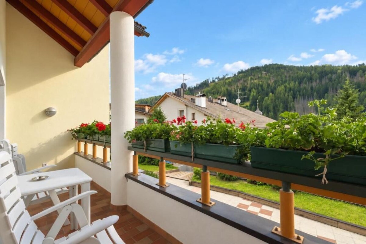 A balcony with a view of a house and forested hills.