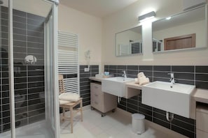 A bathroom with two sinks, a mirror, a towel rack, and a shower area. - Ciasa LaRô (San Cassiano)