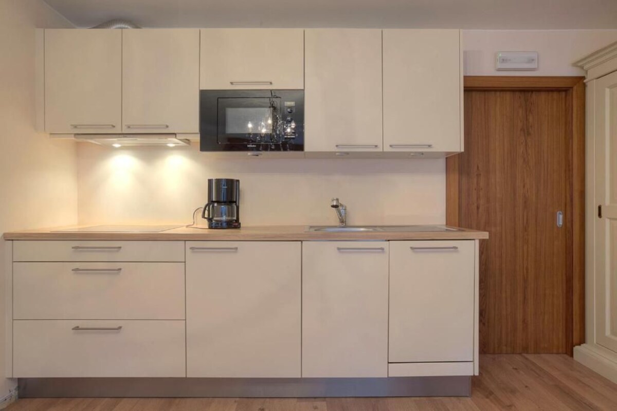 A modern kitchen with white cabinets, a built-in microwave, a coffee maker, and a wooden door.