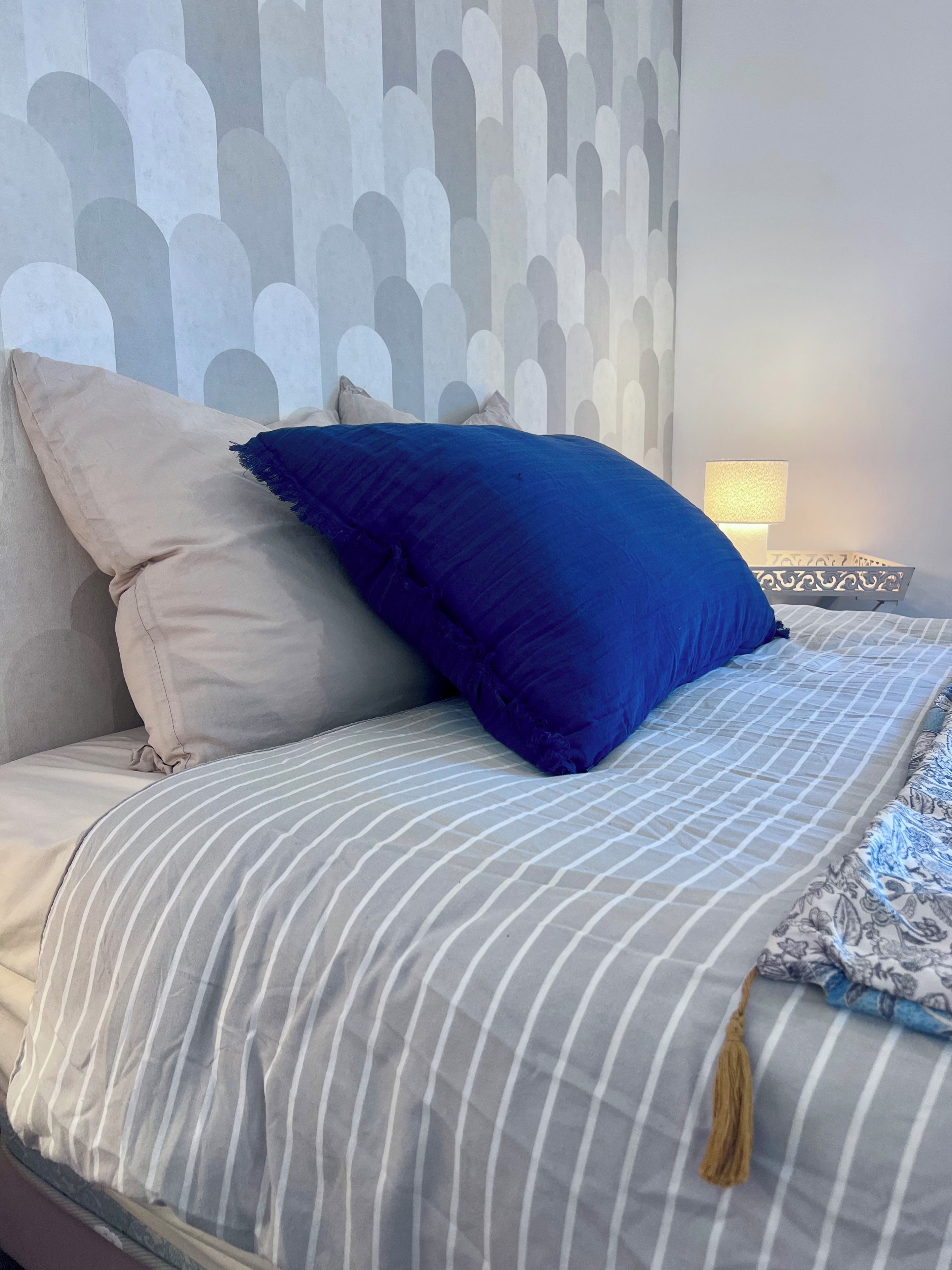 A bed with striped bedding, a blue pillow, and a beige pillow.