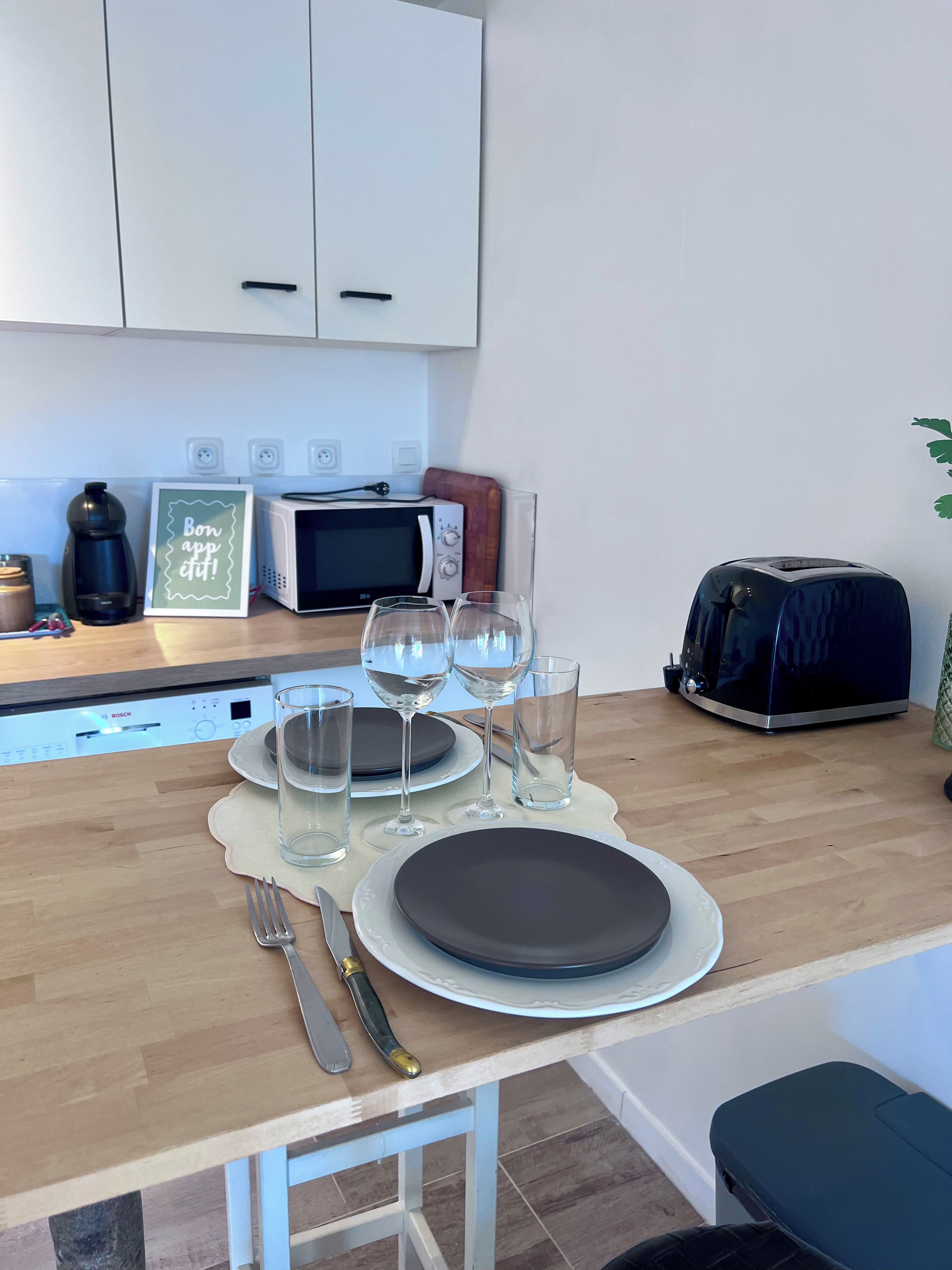A kitchen with a dining table set for two, a microwave, toaster, and a coffee maker.