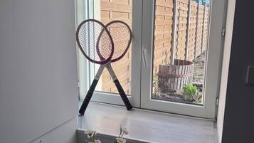 A window sill with two tennis rackets leaning against it and a vase of white flowers below.