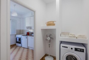 Un área de lavandería con lavadora, un ventilador y un estante con toallas dobladas.