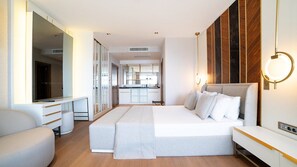 Una habitación de hotel moderna con una cama grande, un televisor, un escritorio y una kitchenette al fondo.