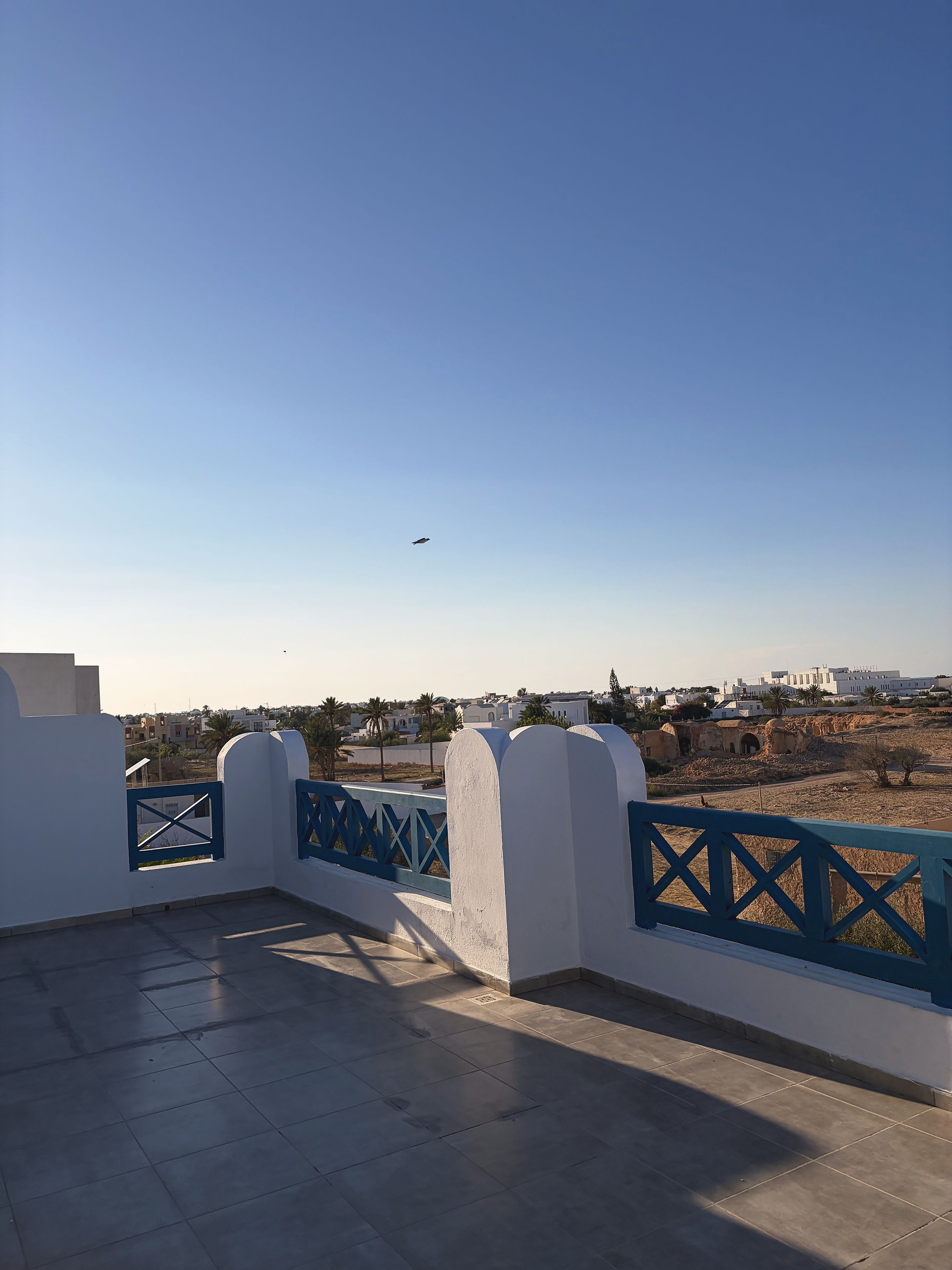 A balcony with a clear view of a distant cityscape, including buildings and palm trees.
