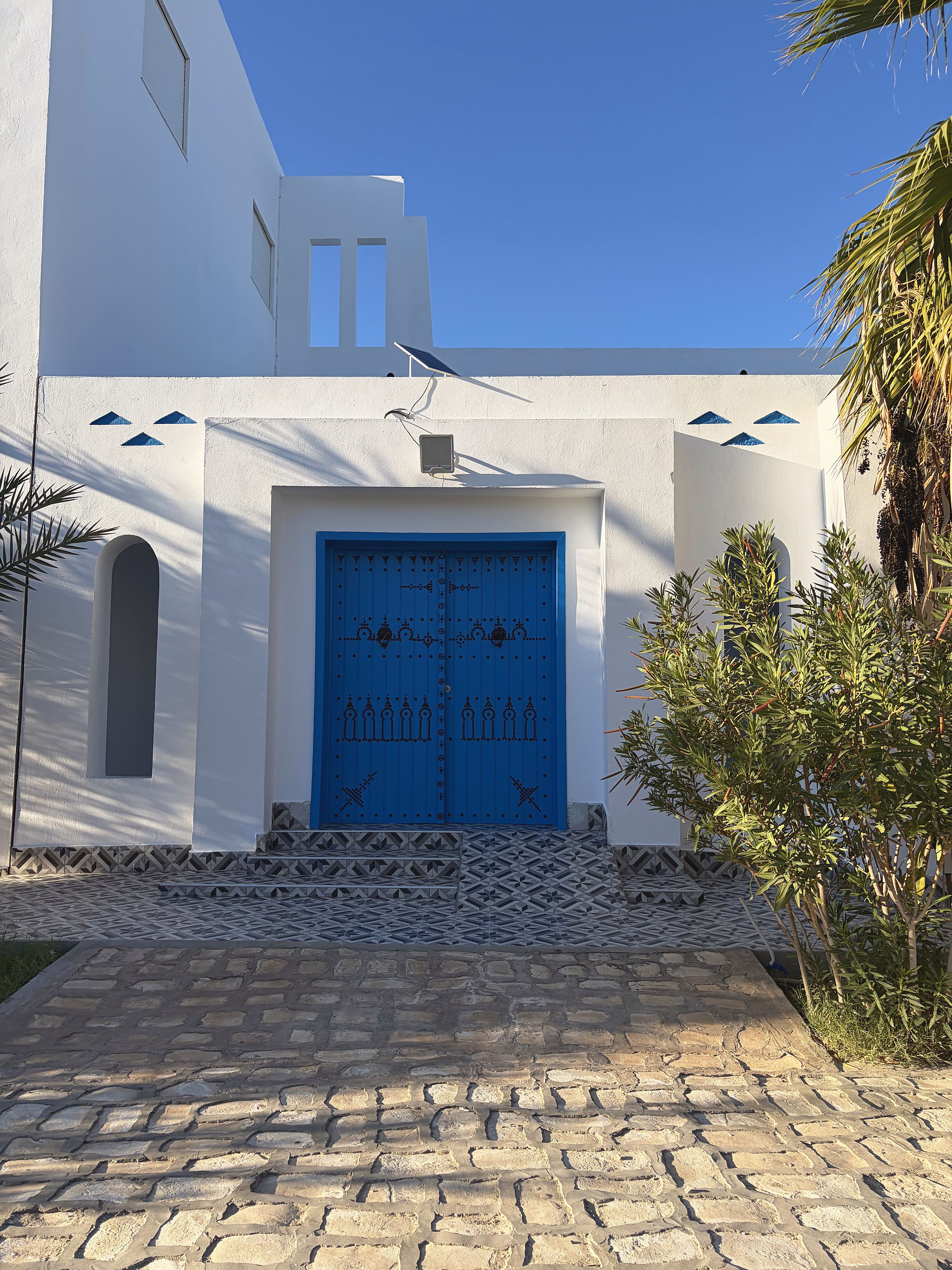 A building with a blue door, white walls, and a stone-paved entrance.