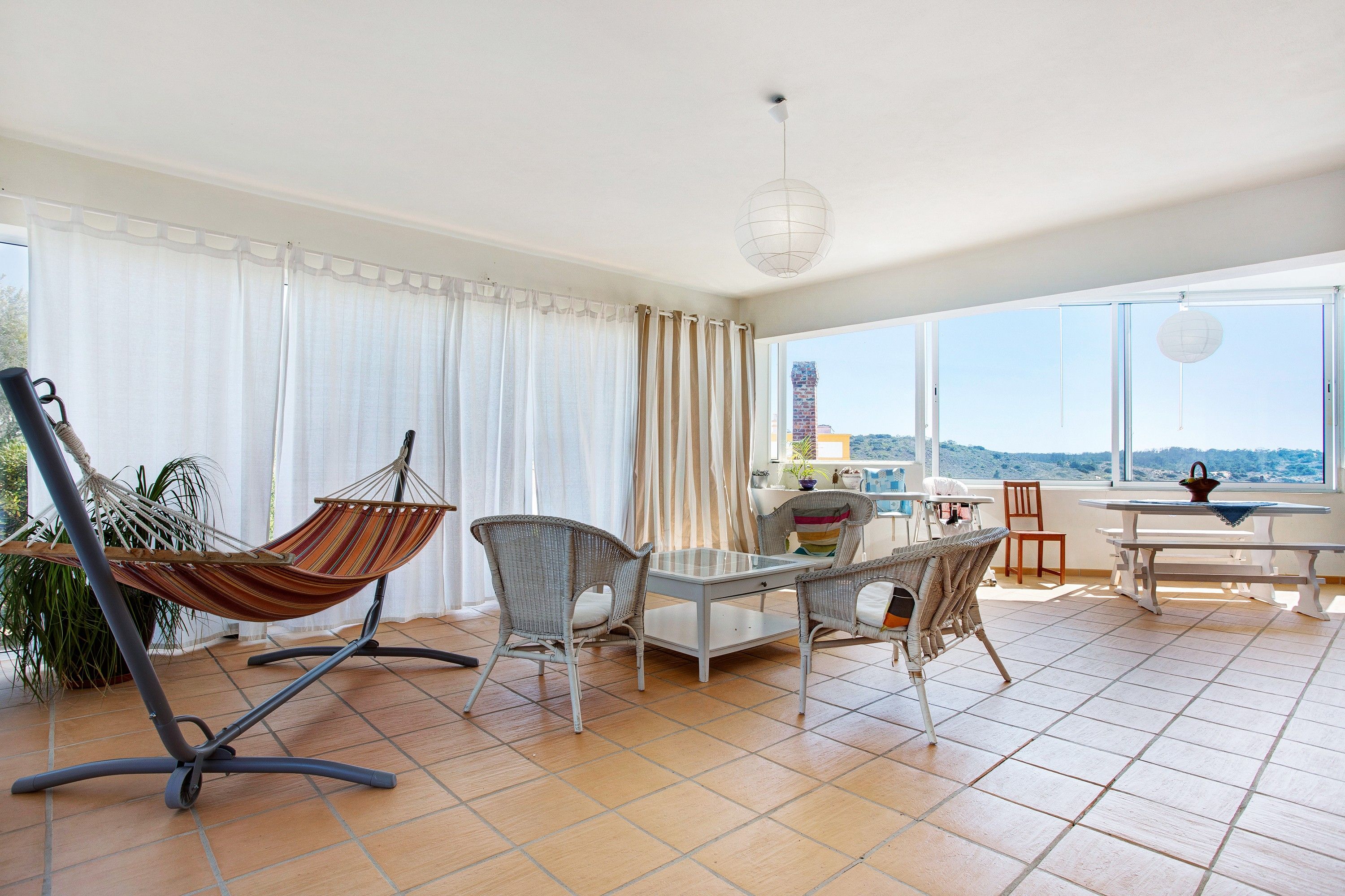 Un balcon spacieux avec un hamac, des fauteuils en osier, une table à manger et une vue sur une tour lointaine.