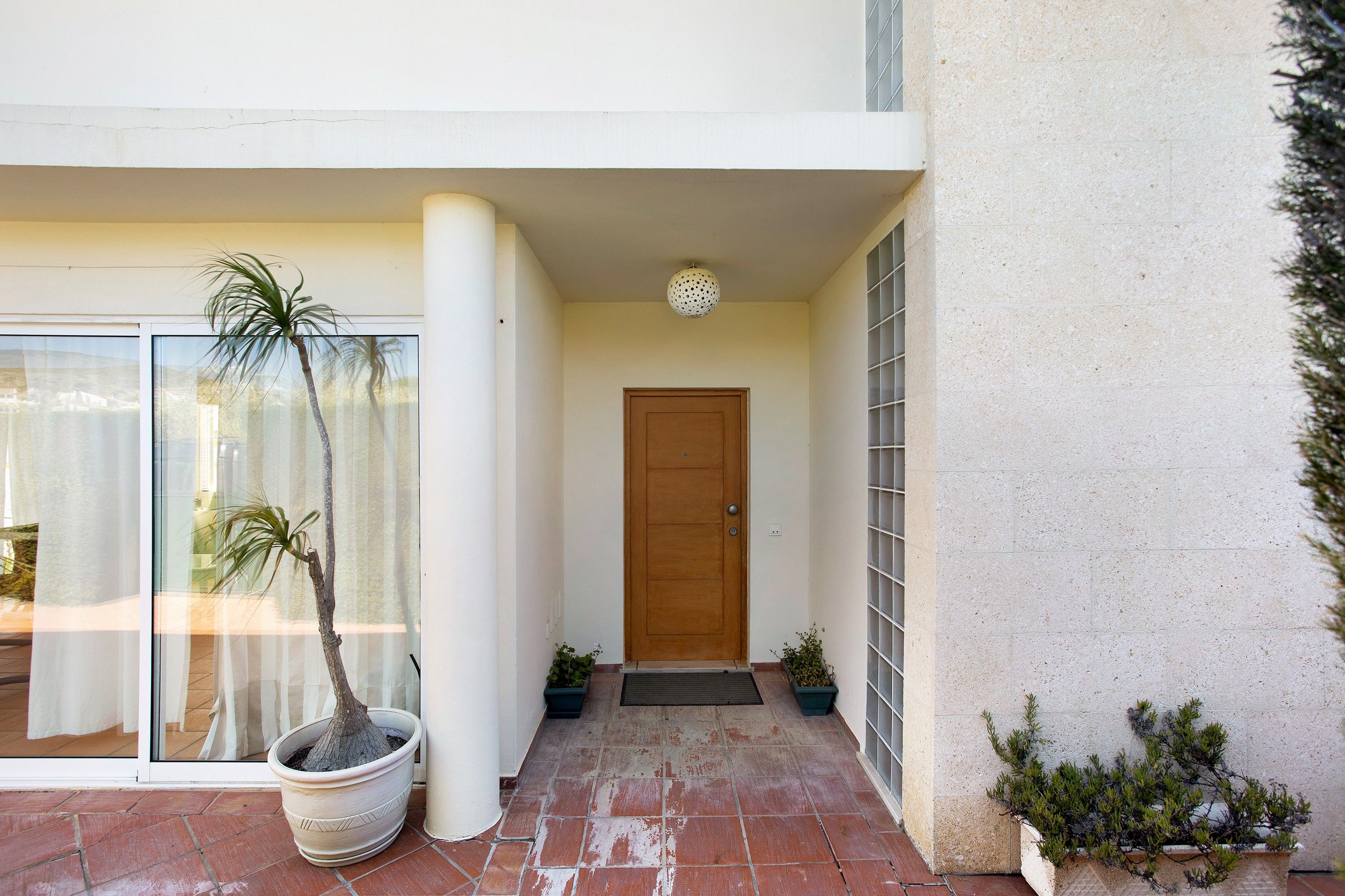 Una entrada de edificio con puerta de madera, plantas en macetas y puerta de cristal que da a un patio.