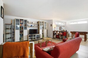 Un salón con un sofá rojo, un televisor y una estantería llena de libros y objetos decorativos.