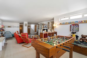Una sala de estar con una mesa de fútbol de mesa, una silla roja, un sofá y una estantería.