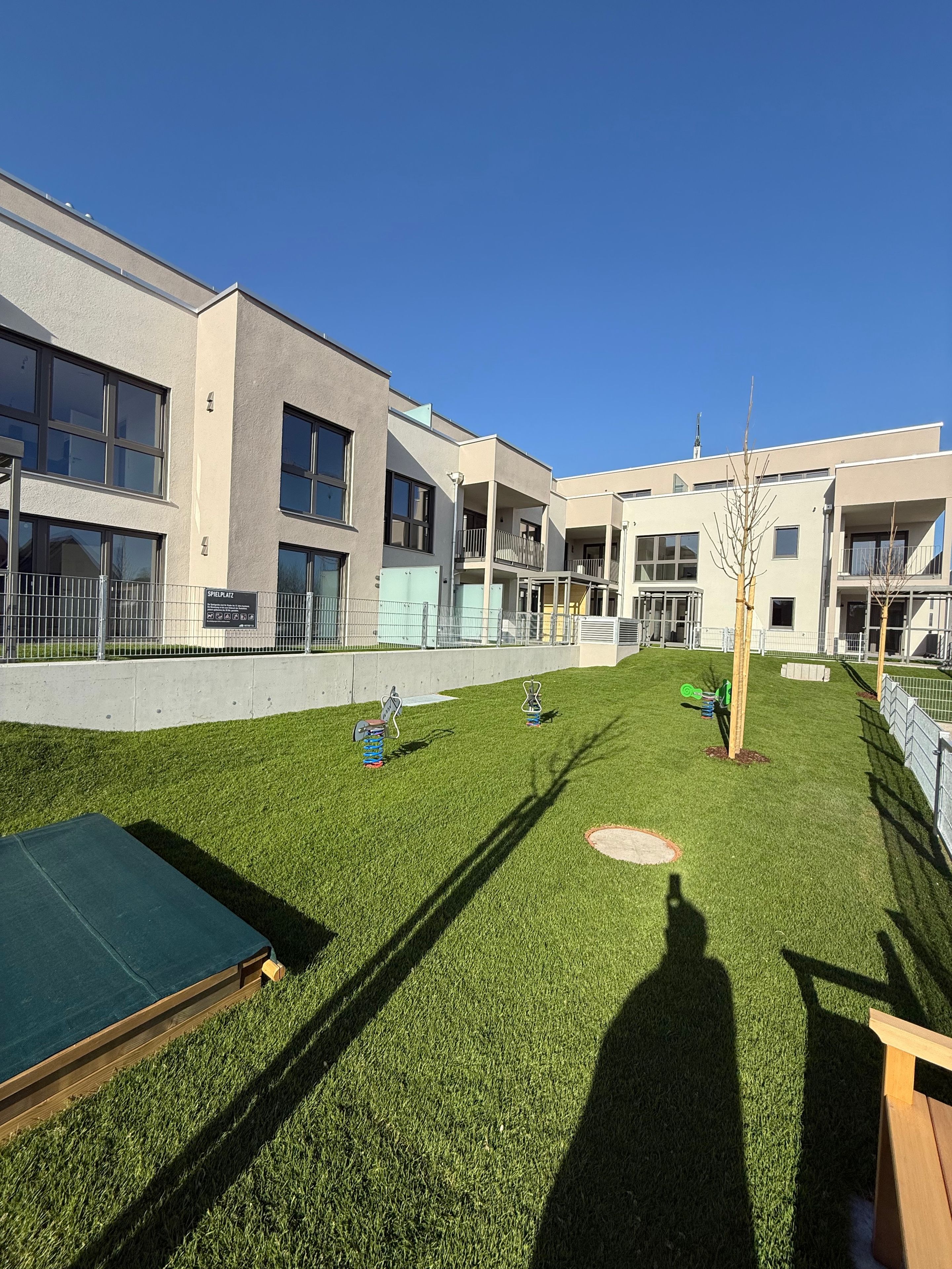Une cour avec une pelouse artificielle, des jeux pour enfants et un bâtiment doté de nombreuses fenêtres et de balcons.