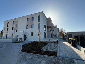 Un edifici modern amb diversos pisos, un terrat pla i un passeig pavimentat que condueix a una entrada tancada.