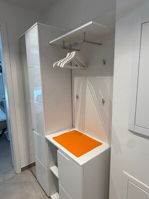 Habitació compacta amb armari integrat, una petita zona de seients amb un coixí taronja i una prestatgeria per a la roba.