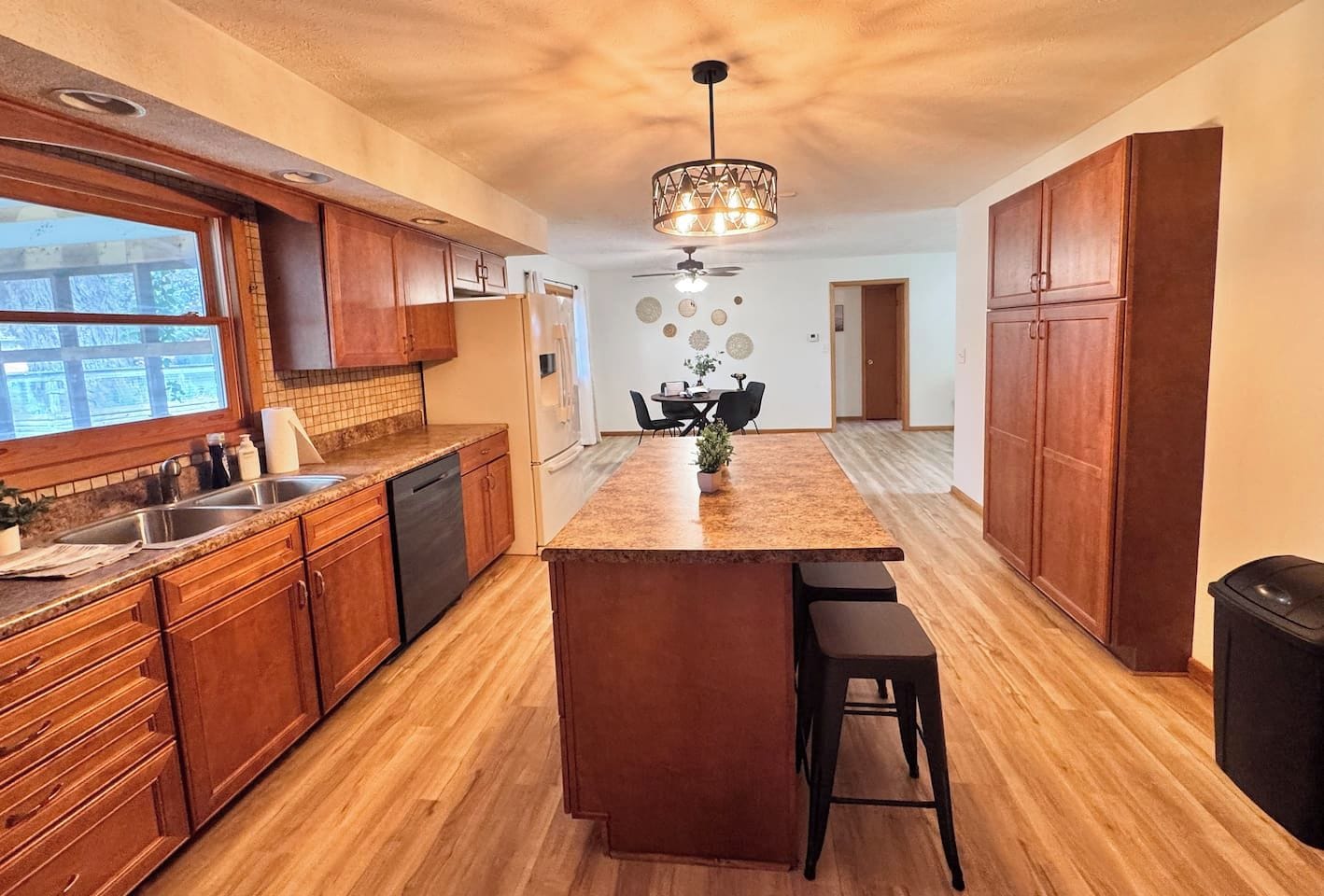 A kitchen with wooden cabinets, a granite countertop, a central island with stools, and a ceiling fan.