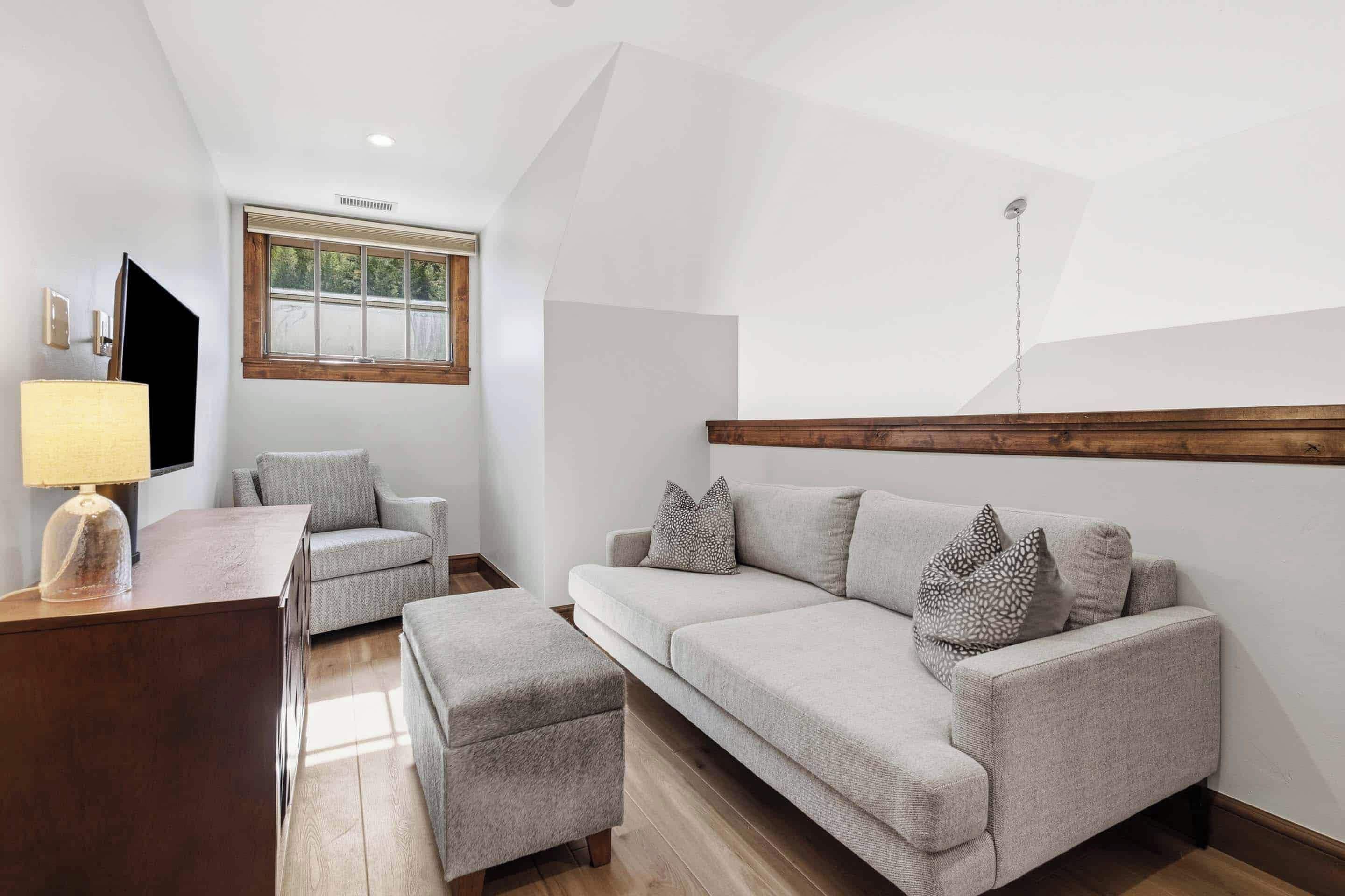 Un salon moderne avec un canapé, un pouf et un téléviseur.