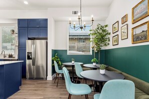 Eine moderne Küche mit einem Edelstahl-Kühlschrank, blauen Schränken und einem Essbereich mit runden Tischen und hellblauen Stühlen.