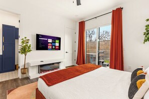 Ein modernes Schlafzimmer mit Bett, einem flachbildfernseher an der Wand, einem Kamin und einem Balkon mit roten Vorhängen.