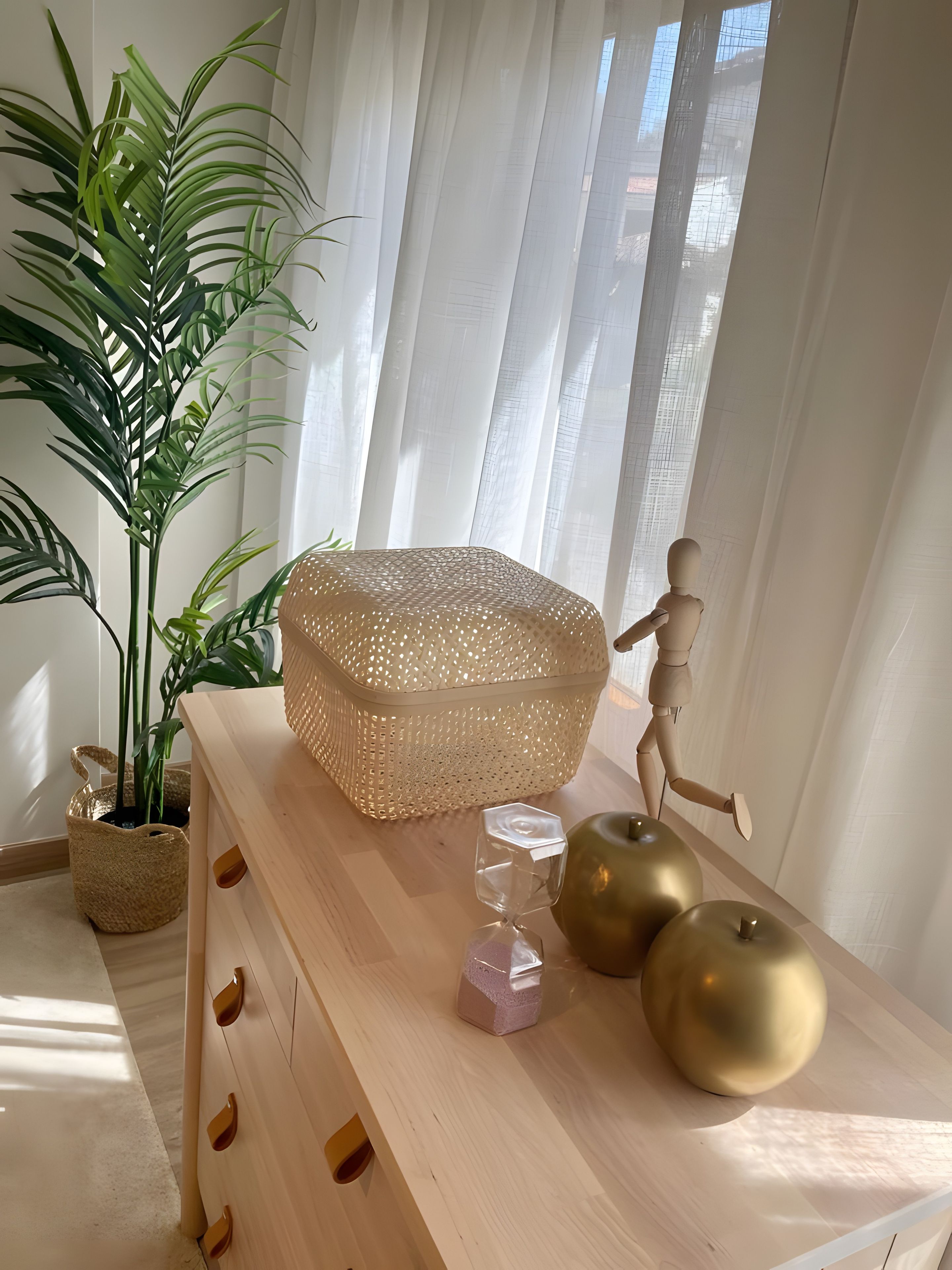 Une commode en bois avec des tiroirs, un panier en osier, un vase en verre et deux pommes dorées.