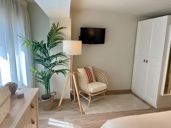 Ein Hotelzimmer mit Bett, Wandfernseher, Blumentopf, Korbsessel und Kleiderschrank.