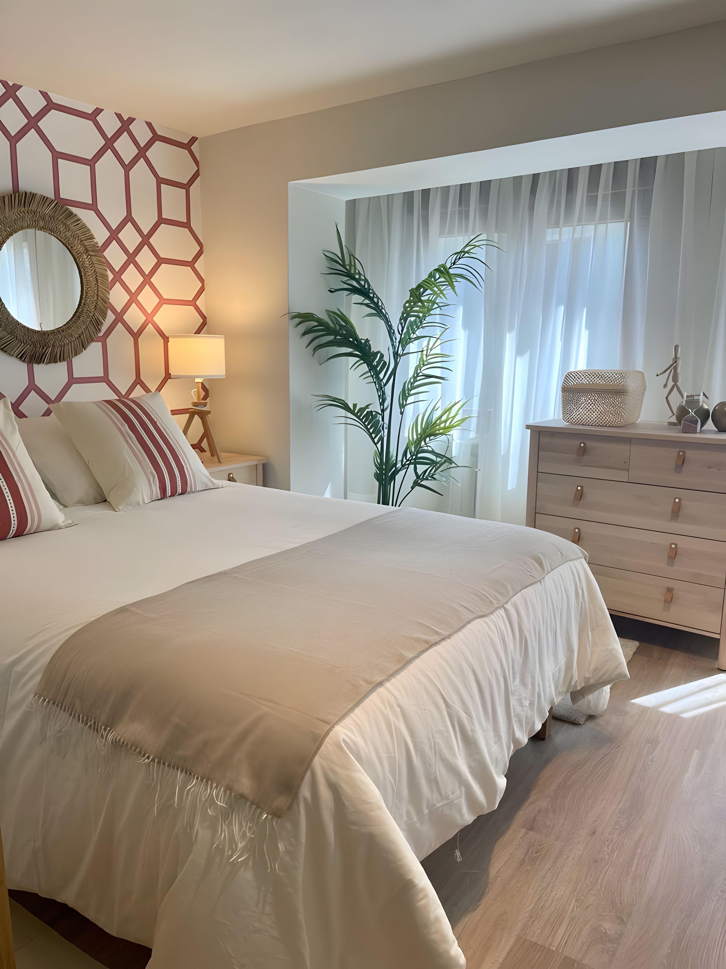 Un dormitorio con una cama grande, una mesita de noche con lámpara, un aparador y una ventana con cortinas traslúcidas.